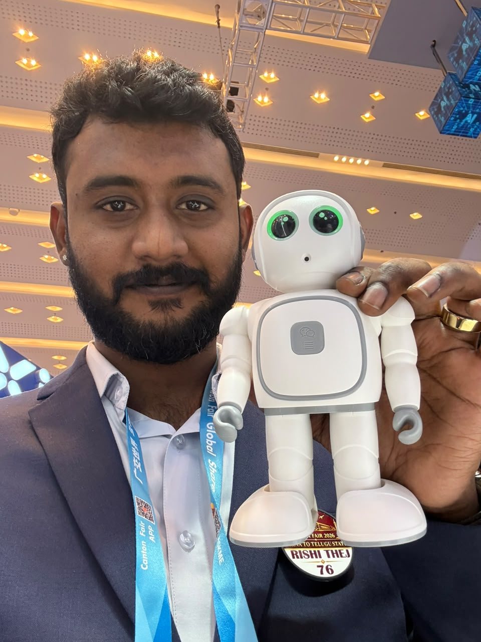 Bollam Rishithej holding a small white companion robot with large green eyes at the Canton Fair in Guangzhou