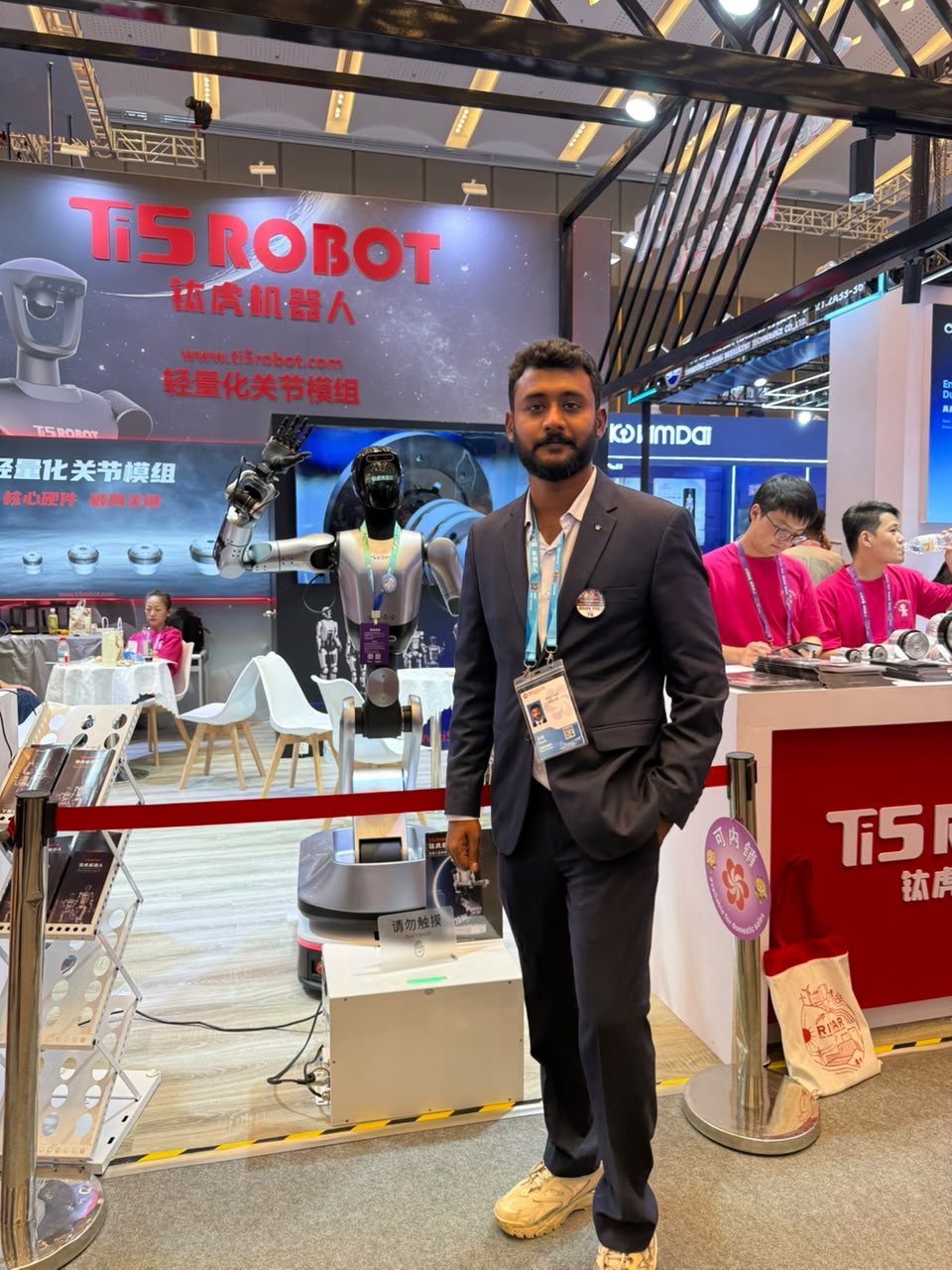 Bollam Rishithej at the Ti5 Robot booth at the 140th Canton Fair in Guangzhou, beside a humanoid robot with its arm raised