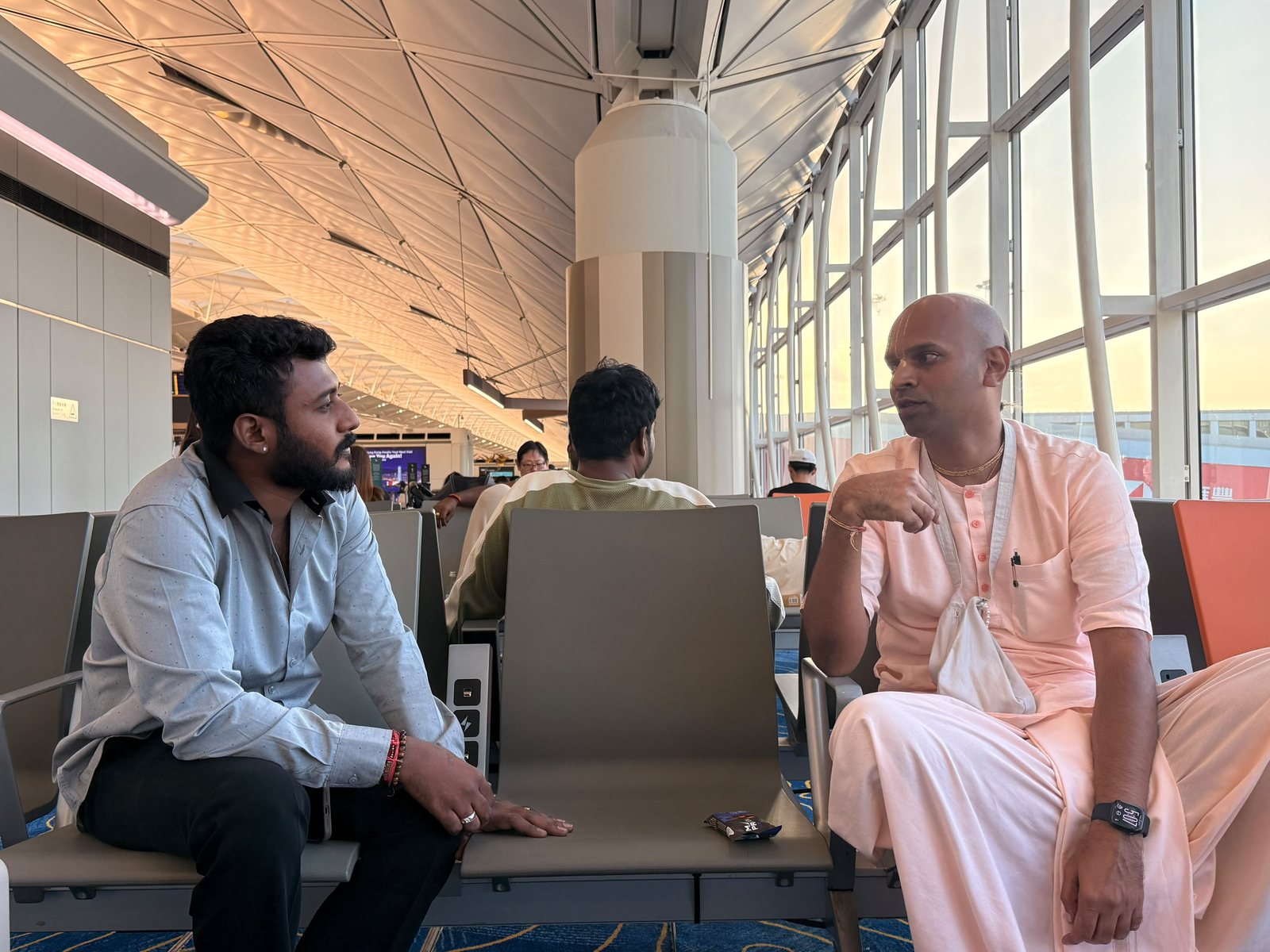 Bollam Rishithej in conversation with a monk of ISKCON at a departure gate at Hong Kong International Airport